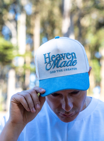 Person wearing a blue and white cap with 'Heaven Made God the Creator' text, outdoors.
